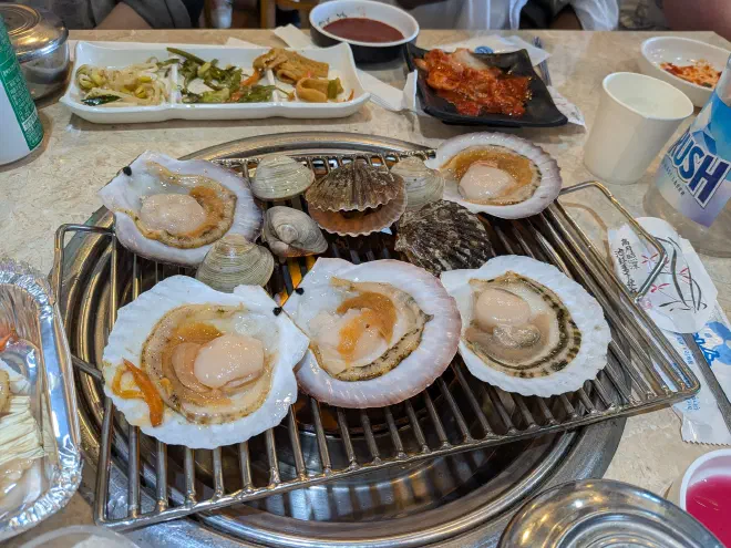 Clams being cooked over a grill in the middle of a table covered by plates