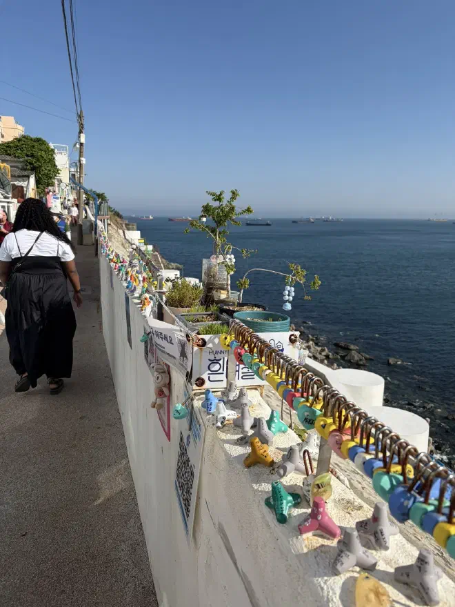 A wall next to the ocean covered in locks and small painted knick-knacks