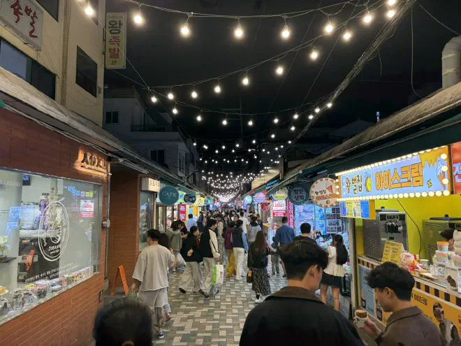 A narrow street adorned with string-lights, packed with people