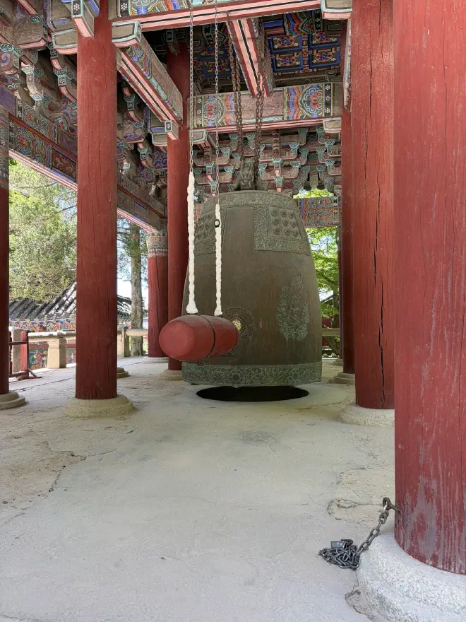 A very large bell A large weathered bell hanging in a wooden building with red pillars and a painted ceiling
