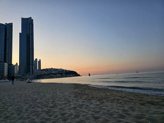 Sunrise over Haeundae beach Sun rises in the distance behind two high-rise buildings