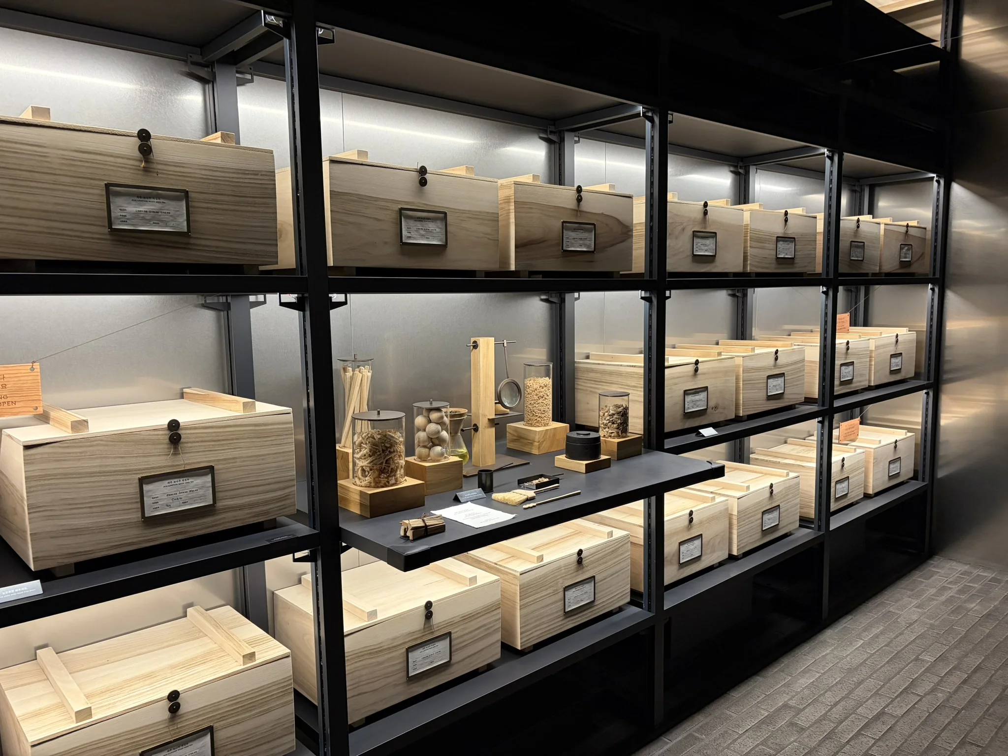 Boxes of Tea in the 'Vault' Multiple boxes on a metal rack with brass labels alongside glass containers holding dried botanical samples and traditional herbal materials