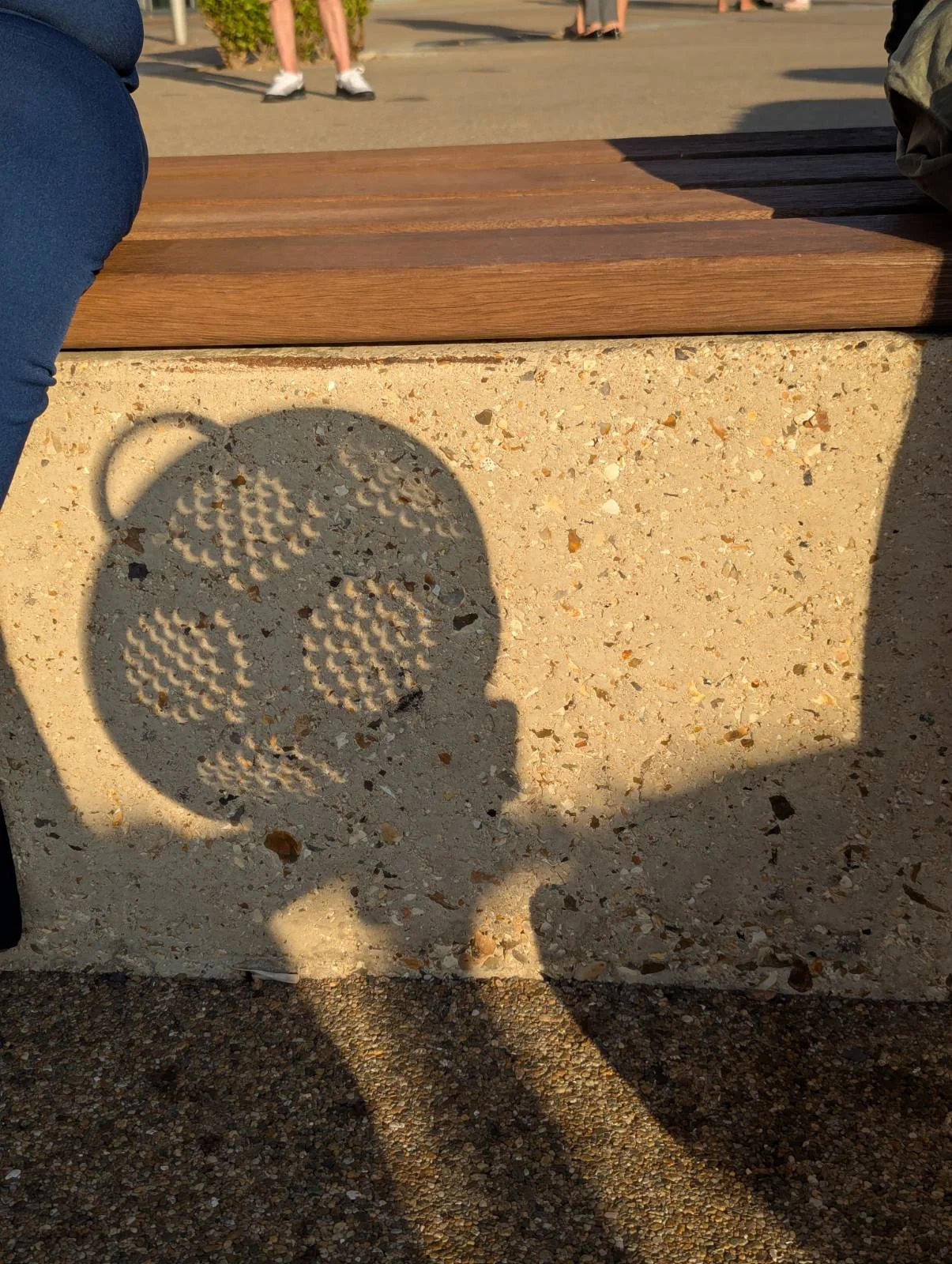 A strained eclipse A colander projecting cresent suns onto a stone bench