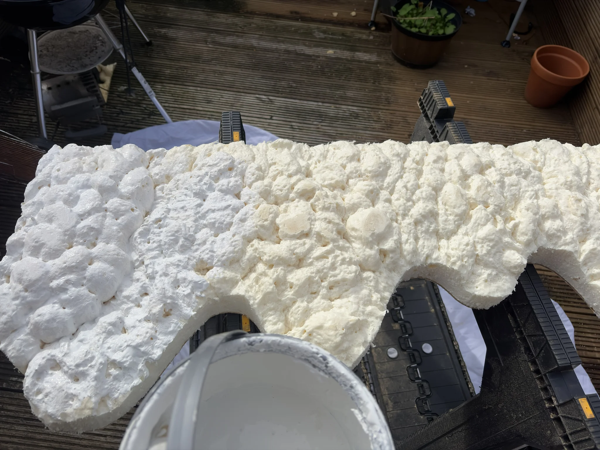 Painting Christmas Spray foam on wood partially painted white sits on trestles on a wooden deck
